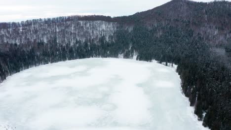 Volcanic-Crater-Lake-Of-Saint-Anne-Covered-In-Ice-And-Surrounded-With-Pine-Forest-At-Winter-In-Harghita,-Romania