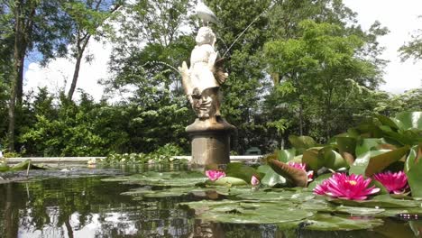 Pink-Waterlilies-Floating-On-Pond-Water-With-Statue-Fountain-At-The-Rotterdam-Zoo-In-Netherlands
