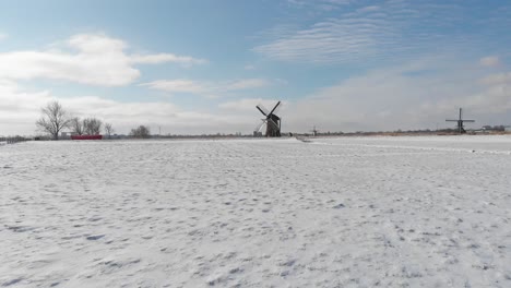 Dutch-winter-windmill-snow-scene,-dolly-aerial-flight-over-field