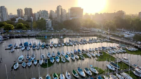 Aerial-dolly-in-of-yachts-docked-inline-in-Olivos-Port-leading-to-expensive-buildings-in-background-at-sunset,-Buenos-Aires