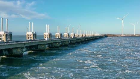 Aerial-shot-of-traffic-on-the-Eastern-Scheldt-storm-surge-barrier-and-wind-turbines-in-Zeeland,-the-Netherlands,-on-a-beautiful-sunny-day