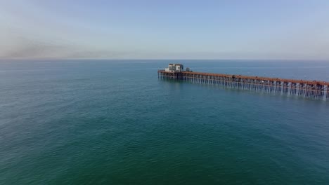 drone-forwards-over-ocean-water-toward-wooden-pier-in-Oceanside,-south-California,-United-States
