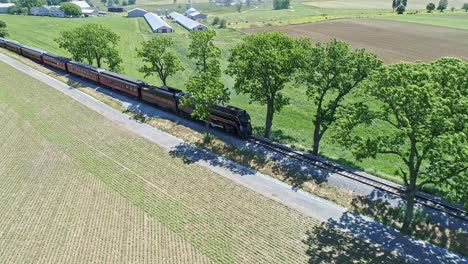Eine-Drohnenansicht-Einer-Dampflokomotive-Mit-Personenwagen,-Die-Sich-An-Einem-Schönen-Sommertag-über-Die-Landschaft-Nähern