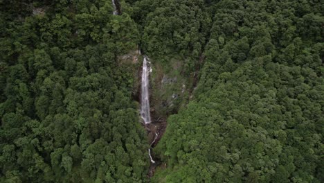 Majestic-tropical-waterfall-inside-rich-green-forest-in-Switzerland,-aerial