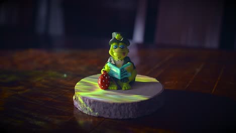 Ceramic-Frog-Reading-Newspaper,-Sitting-On-Wooden-Presentation-Base-Against-Spotlight