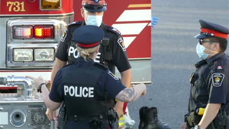 Polizisten-Tragen-Masken-Und-Unterhalten-Sich-Mit-Einem-Feuerwehrauto-Im-Hintergrund