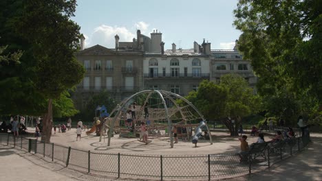 Panning-across-playground-area-with-kids-playing-on-climbing-dome-on-sunny-day-in-Parc-Monceau-in-Paris,-France