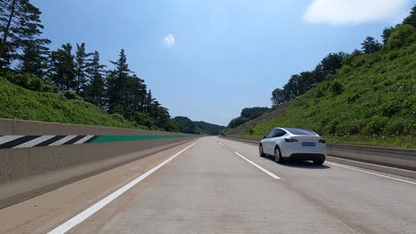Día-Soleado-En-La-Carretera-Con-Vista-A-Un-Tesla-Blanco-Modelo-Tres-Automóviles