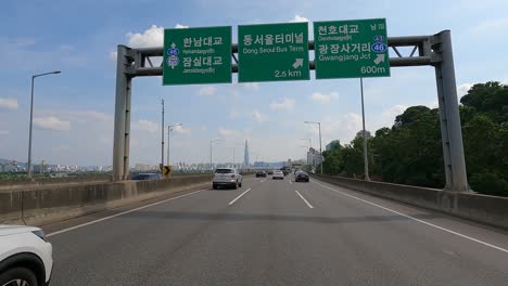 Driver's-POV-on-Gangbyeonbuk-ro-road-near-Han-river,-Lotte-Tower-on-background-Seoul,-Korea,-Jun-27,-2021-summer-day-cloudy
