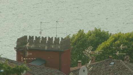 Slow-motion-shot,-a-bird-flying-through-the-top-of-the-roof-top-in-Malcesine-in-Italy,-Lago-di-Garda-in-the-background