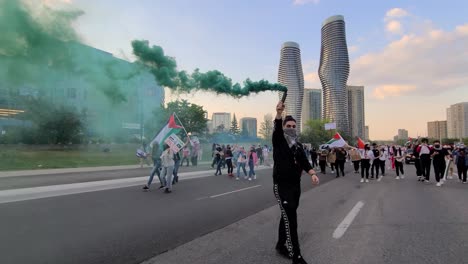 A-demonstrator-holding-green-smoke-bomb-for-pro-Palestinian-rally-in-Mississauga-with-the-rest-waved-their-Palestinian-flags-in-the-background-to-create-awareness-of-Israelâ€“Palestine-conflict
