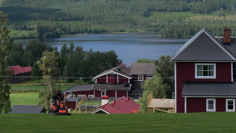 Man-Mows-Lawn-In-A-Traditional-Village-In-Northern-Sweden,-Lake-Landscape-In-Background
