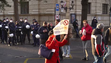 Mujer-De-Mediana-Edad-Sosteniendo-Un-Cartel-Antivacunas-Caminando-Frente-A-La-Policía-Durante-Las-Protestas