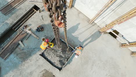 POV-top-down,-construction-workers-connecting-tower-crane-chains-to-container-full-of-gravel-at-a-construction-site