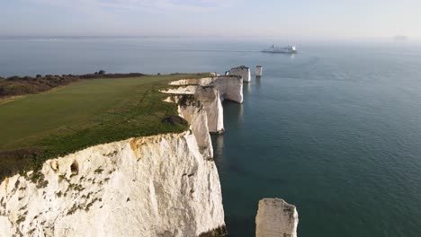 Aerial-forward-over-white-and-jagged-cliffs-of-Old-Harry-Rocks-and-ship-cruising-in-background,-Purbeck-island,-Dorset