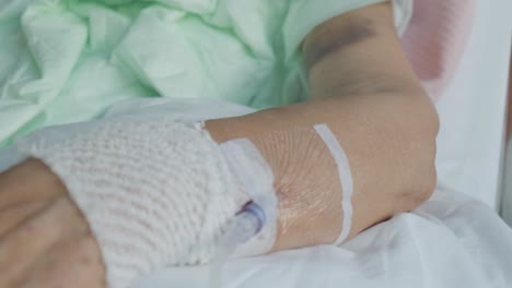 Close-up-Motion-through-aged-patient-Hospital-bed,-Intravenous-solution-tubes-and-bruised-arm