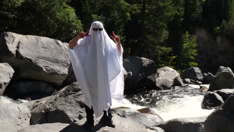 Dressed-up-as-a-ghost-holding-up-a-peace-sign-next-to-a-flowing-river