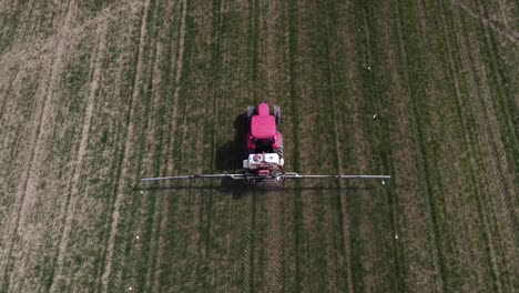 Aerial-view-of-red-farming-tractor-spraying-on-the-cultivated-field-with-sprayer,-herbicides-and-pesticides-insecticide-to-the-green-field-plowed-land