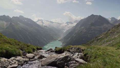 Im-Vordergrund-Fließt-Ein-Kleiner-Bach-Und-Im-Hintergrund-Die-österreichischen-Alpen-Sowie-Ein-Wunderschöner-Blauer-See
