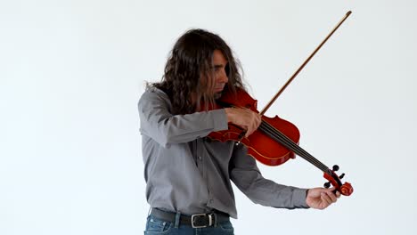 Medium-shot-of-long-hair-latino-male-musician-in-grey-button-up-shirt-and-jeans-tuning-a-red-viola-on-white-backdrop