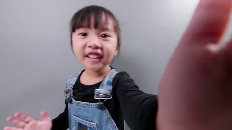 Happy-little-asian-girl-using-smartphone-for-video-call,-waving-hand-and-speaking-and-talking-witn-smile,-greeting-teacher-and-classmates
