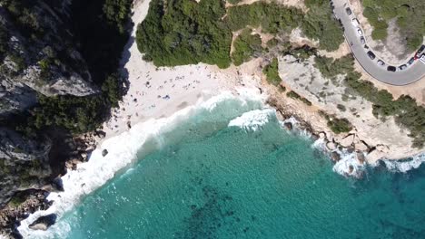 Drone-rises-and-pans-over-the-famous-cala-fuili-bay-in-sardinia-with-a-catamaran-in-crystal-clear-water-and-a-few-waves