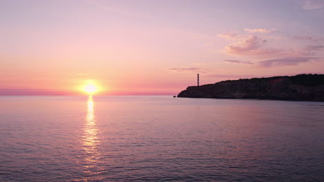 AERIAL---Lighthouse-under-a-pink-and-purple-sunrise-in-Spain,-forward-reveal-shot