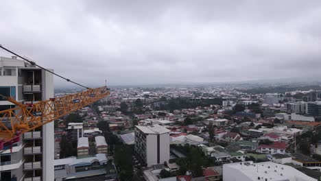 Drone-flying-over-a-crane-building-a-skyscraper-in-San-Jose-city,-Costa-Rica