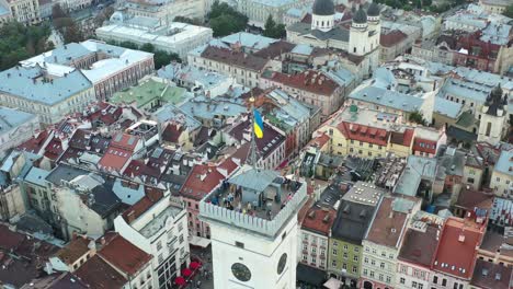 Ukrainische-Flagge-Weht-Auf-Der-Spitze-Eines-Turms-Auf-Dem-Rynok-Platz-In-Lemberg,-Ukraine,-Mit-Europäischen-Gebäuden-Und-Einer-Stadt-Im-Hintergrund
