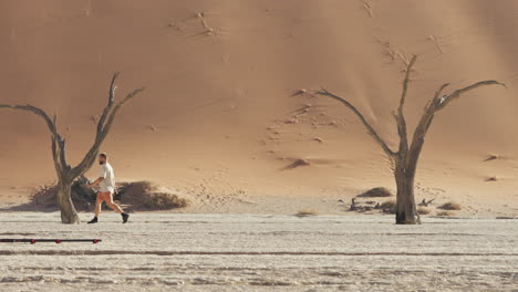 Mann-Geht-Am-Deadvlei-Mit-Toten-Kameldornbäumen-Und-Hohen-Roten-Dünen-Im-Hintergrund