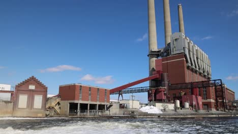 Coal-burning-power-plant-with-three-smoke-stacks-panning-to-river-dam