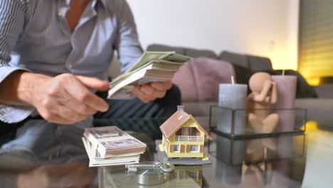 Close-up-shot-of-Man-counting-cash-money-on-table-at-home-for-buying-own-real-estate-with-villa