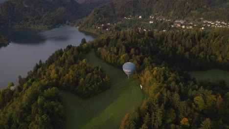 Balloon-trip-rising-from-rural-field-near-lake-Bled-in-morning,-aerial