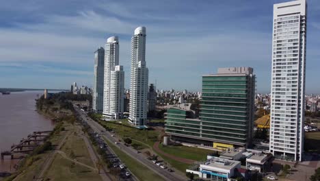 Beautiful-architectural-view-of-Rosario-from-a-drone-on-a-sunny-day-along-the-ParanÃ¡-coast-with-cars-crossing-the-riverside-street