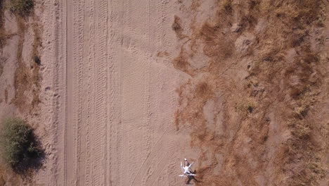White-Consumer-Drone-Sits-Along-Sandy-Desert-Road-Path-Before-Launch