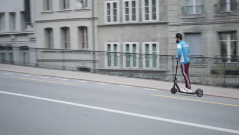 View-of-a-young-guy-passing-by-on-a-two-wheeler-standing-electric-scooter-on-the-streets-in-Fribourg,-Switzerland-on-the-cloudy-day