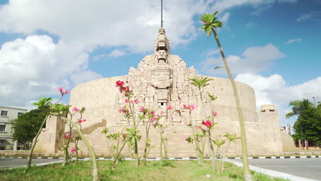 Rotonda-Del-Monumento-A-La-Patria-En-El-Centro-De-Mérida,-México,-Con-Flores-Rosas-Y-Tráfico.
