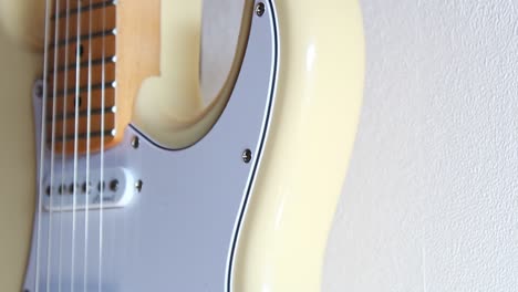 Close-up-footage-of-a-cream-white-stratocaster-hanging-off-a-white-interior-wall