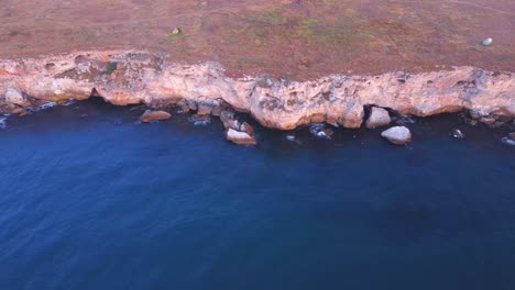 Top-down-aerial-view-of-waves-splash-against-rocky-seashore,-background