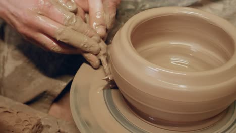 Apprentice-scraping-off-excess-clay-with-triangle-knife-on-ancient-revolving-pottery-wheel