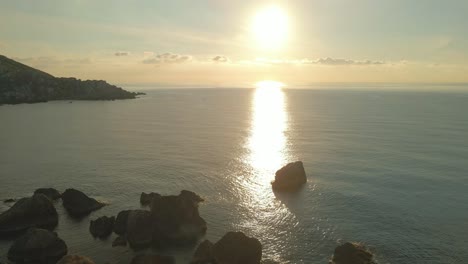 Luftaufnahme-Eines-Malerischen-Sonnenuntergangs-Im-Mittelmeer,-Mit-Großen-Felsen-Im-Wasser-Und-Der-Sonne,-Die-Sich-Auf-Der-Meeresoberfläche-Spiegelt,-Malta