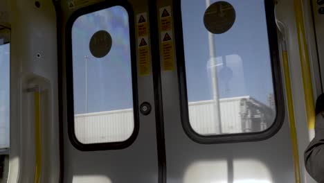 Inside-View-Looking-At-Double-Doors-Of-S8-Stock-Metropolitan-Train-As-It-Goes-Past-Buildings-And-Blue-Sky