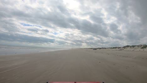 POV-thru-windshield-of-vehicle-driving-on-beach-between-surf-and-dunes-of-North-Padre-Island-National-Seashore-near-Corpus-Christi-Texas-USA-on-a-cloudy-day