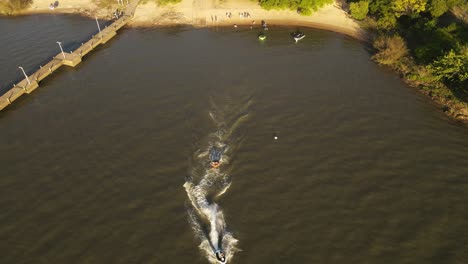 Drohnenaufnahme-Eines-Jetskis,-Der-Ein-Schlauchboot-Auf-Dem-Wasser-Fährt,-Wunderschöner-Sommersonnenuntergang-Bei-Fray-Bentos,-Uruguay