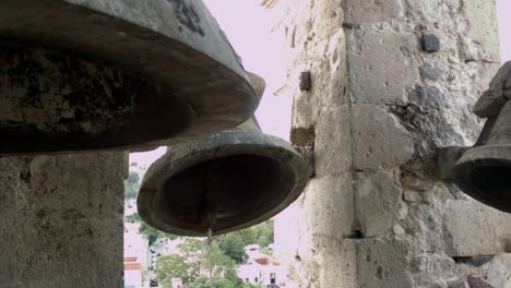 Church-bells-mounted-in-high-tower-in-the-public-square-of-a-small-mexican-town,-that-can-be-heard-by-the-surrounding-community