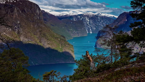 High-angle-timelapse-shot-over-the-lake-in-the-valley-with-snow-covered-mountain-range-all-round-in-Flam,-Norway-on-a-cloudy-day