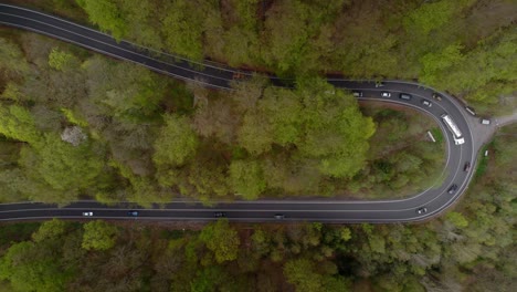 Passing-cars-and-truck-in-a-winding-road-in-the-mountains-in-the-middle-of-wooded-nature---bird's-eye-view-down