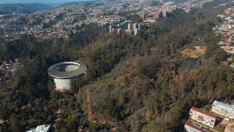 Aerial-dolly-out-of-Quinta-Vergara-Amphitheater-in-Park-covered-in-woods,-Viña-del-Mar-hillside-city-in-background,-Chile