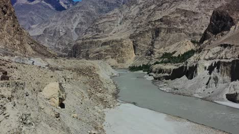 Luftdrohne-Fliegt-über-Eine-Bergklippe-In-Richtung-Des-Schnell-Fließenden-Grauen-Indus-Flusses-In-Skardu,-Pakistan,-Mit-Blick-Auf-Die-Großen-Berge-An-Einem-Sonnigen-Sommertag