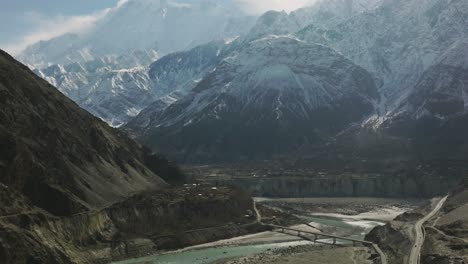 Filmische-Luftaufnahme-Des-Flusses-Hunza-Valley-Mit-Nach-Oben-Geneigter-Sicht-Auf-Schneebedeckte-Berge